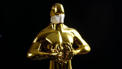 Hollywood Golden Oscar Academy award statue in medical mask on black background with copy space. Success and victory concept. Oscar ceremony in coronavirus time