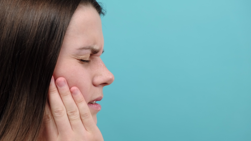 Close up of young brunette woman suffering from toothache, isolated on blue studio background. Causes of tooth pain include tooth decay, inflammation, dental abscess, gum disease or sensitive teeth Royalty-Free Stock Footage #1084808461