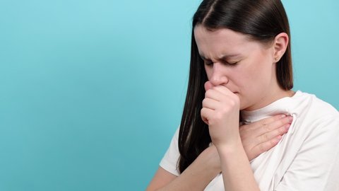 Ill young female 20s have cough and sore throat, isolated over blue background with copy space. Causes of cough include pneumonia, bronchitis, allergy, asthma, COPD, TB or respiratory tract infection