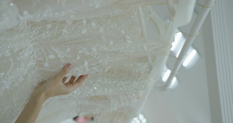 beautiful female hand examines the corset of a wedding dress on a hanger. The hand of the designer is touching the dress in production. Beautiful shiny fabric. Vertical video. Large lpan