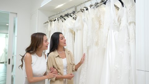 4K Beautiful Asian woman lesbian couple choosing wedding dress for marriage ceremony in bridal shop together. Diversity sexual equality, lgbtq pride, marriage equality and Same-sex marriage concept.