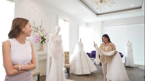 4K Beautiful Asian woman lesbian couple choosing wedding dress for marriage ceremony in bridal shop together. Diversity sexual equality, lgbtq pride, marriage equality and Same-sex marriage concept.