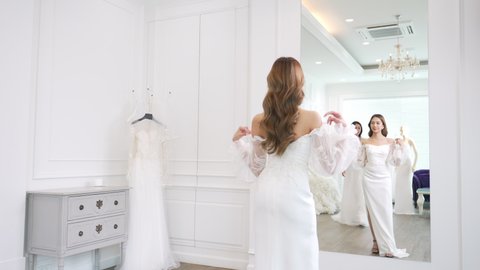Asian woman lesbian couple choosing and trying on wedding dress for marriage ceremony in bridal shop together. Diversity sexual equality, lgbtq pride, marriage equality and Same-sex marriage concept.