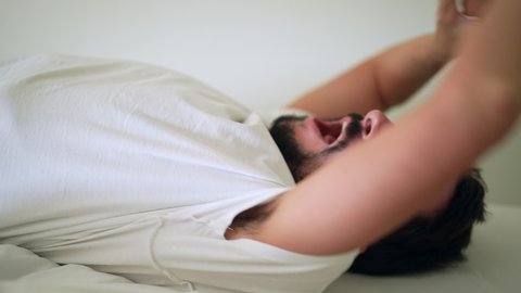 Man yawning waking up from nap, person lying in bed yawns