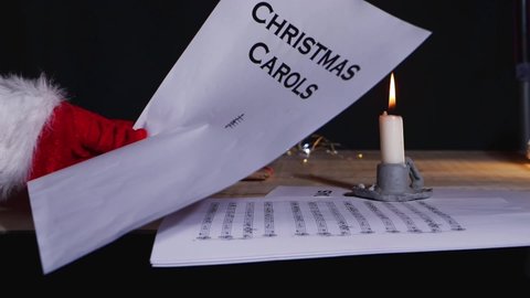 Hand holding Christmas carols music song sheet by candlelight close up slow motion shot selective focus