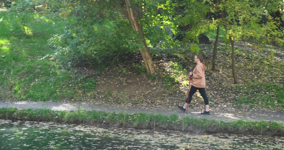 Young woman walking with hiking poles by lake