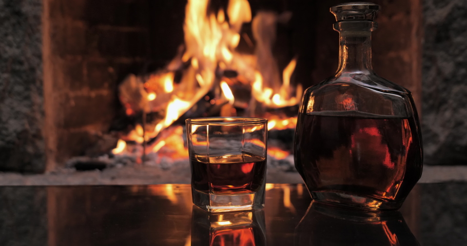 Bottle and glass with whiskey or cognac. Burning Fire In The Fireplace. Warmth and home comfort. 4K