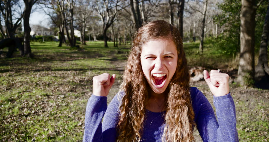 Excited young beauty in park cheering and waving triumphantly, in slow motion
