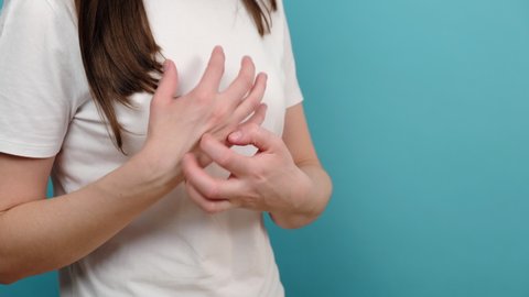 Close up of young woman scratching itch on hands, redness rash, isolated on blue studio background with copy space. Causes of itchy skin include dermatitis, burned, food drugs allergies, insect bites
