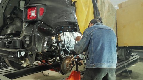 Unrecognizable mechanic using welding in a garage, repairing a car body, recovering from an accident