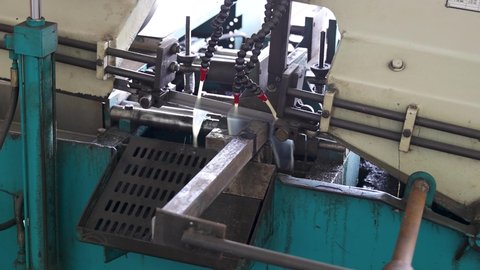a square pipe is being cut off in a hacksaw or bandsaw machine in a factory