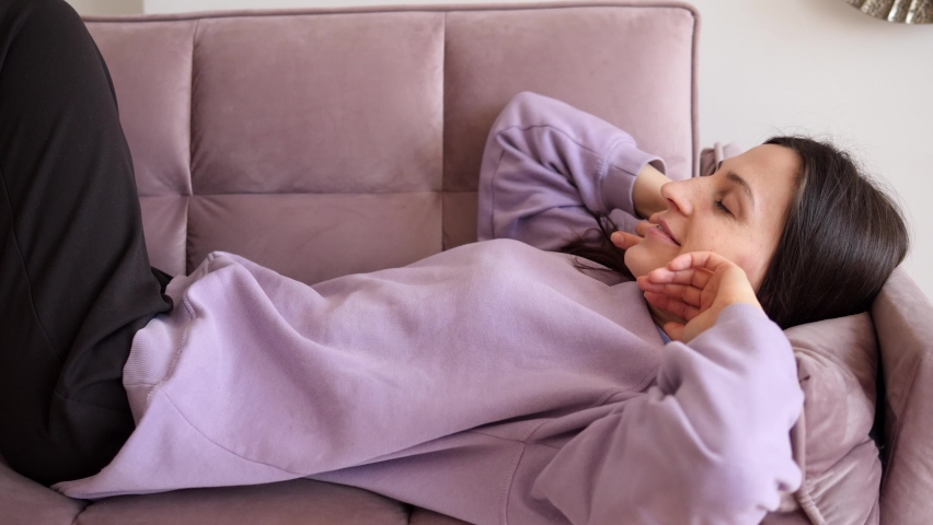 Bored young sleepy woman relaxes on the couch. An apathetic, tired, lazy lady sleeps on the couch at home alone. Lack of motivation, fatigue or depression concept | Shutterstock HD Video #1084830415