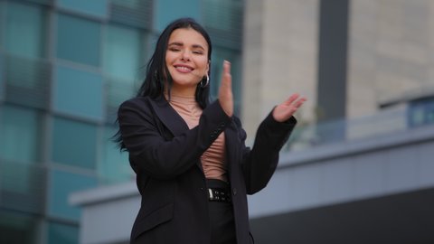 Enthusiastic young businesswoman standing on city building backround smiling clapping hands hispanic girl looking at camera applauding expresses approval admiration ovation greeting congratulations