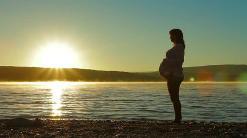 Belly of a pregnant woman silhouette in the sun. Woman showing hand class.