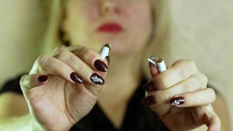 Portrait of a blonde Caucasian woman over 40 years old holding a peed on her face and breaking a cigarette. The woman stops smoking. Quit smoking, give up bad habit. selective focus