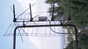 VERTICAL VIDEO: Old, Rusty TV Antenna is Attached to a Bracket Outside Window. A metal outdoor antenna is behind balcony a blurry background of sky, trees, clouds. Signal reception. Building facade.