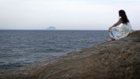 Blurred defocused Beautiful young asian woman sitting on the rock of beach, looking at wild rocky coastal landscape of Yehliu Geopark in New Taipei City, Taiwan