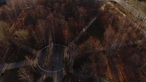 Empty playground and paved roads in small city park with high bare trees at sunset in nice autumn evening bird eye view