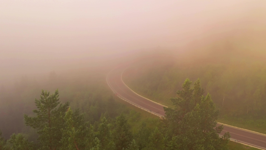 The drone flies over the road disappearing in a thick fog. Bird