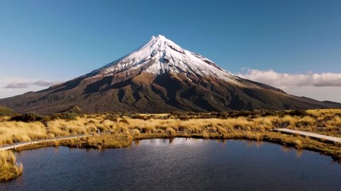 Amazing view of iconic Taranaki volcano aerial reveal of couple tourist photographing over reflection tarn. New Zealand famous travel location.