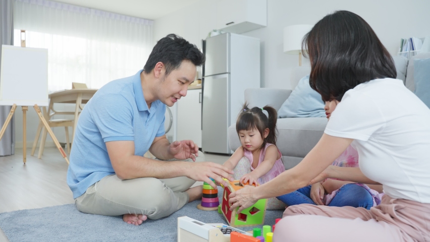 Asian happy family sit on floor, play kid toy together in living room. Attractive parents mother and father spend time with young little girl daughters in house. Activity relationship at home concept.