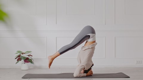 Side view of Asian woman doing Yoga exercise in front of windows,Yoga HandStand pose or Pincha Mayurasana,Calm of healthy young woman breathing and meditation yoga at home