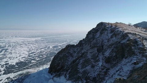 Aerial view of cape Khoboy, Olkhon island. Tall rocks in frozen lake Baikal with many people and cars around. Popular touristic destination. Winter landscape. Panoramic view