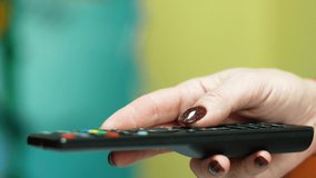 A woman's hand holds a remote control and selects cable TV programs. Smart TV and entertainment content. A woman spends her leisure time watching TV. selective focus