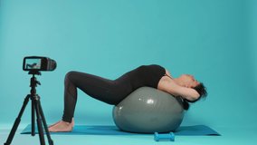 Woman vlogger recording workout video in studio, doing physical muscle exercise on fitness toning ball. Aerobics trainer filming online sport lesson on camera, using gymnastics equipment.