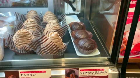 Kasukabe, Saitama, Japan. January 5, 2022. A cake display case with several rum balls,  mont blank, raspberry shortcake,  chocolate cake,  coffee jelly, and almond butter cake at Ueshima Coffee. 