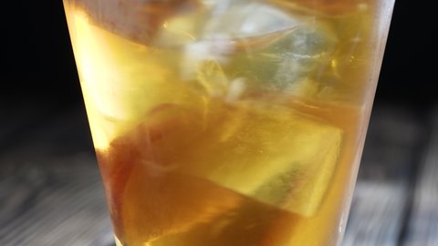 Rotating peach iced tea in the glass with fruit slices and ice cubes. Healthy refreshing lemonade for detoxification, sweet tasty soft drink or cold aromatic beverage for summer time in slow motion