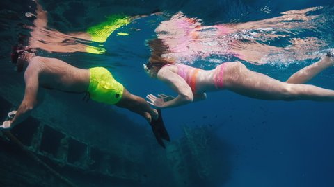 Couple playing underwater. People swimming and snorkelling on the shipwreck in crystal clear water in Maldives and woman playfully pushes the man