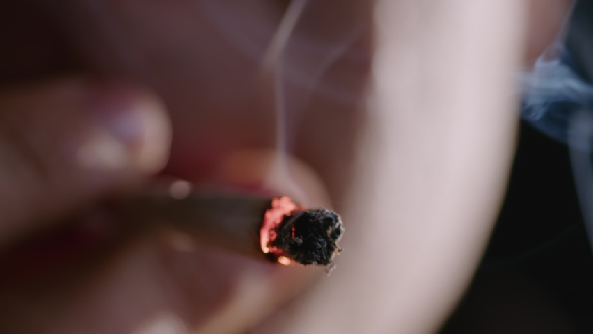 Close-up shot of a burning marijuana joint and blowing smoke into the camera.