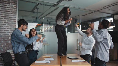 Hispanic businesswoman dancing on table employees have fun conference room celebrating corporate success female leader with colleagues enjoy office party happy diverse business people rejoice victory