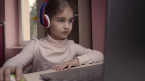 Distance Learning. Schoolgirl Studying Online Using Laptop. School Student Wearing Headphones Watching Internet Course. Future Programmer to Learn Programming. Child Playing on Computer Games.