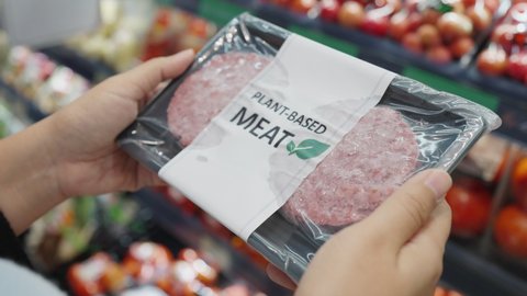 Close-up hand carry choose zero pork soy bean faux peas cutlet gluten free read beyond non-meat lab label. Buy raw fake beef tray in asia store veggie burger patty for health care eat diet meal cook.