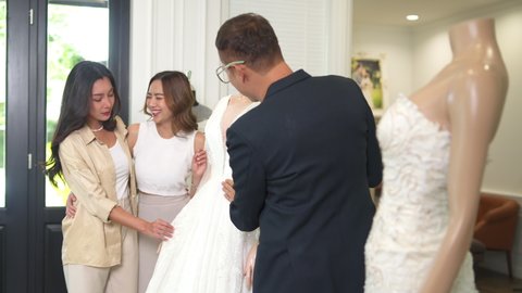 4K Asian LGBTQ guy bridal shop owner helping woman lesbian gay couple choosing wedding gown at wedding studio. Diversity sexual equality, lgbtq pride, marriage equality and Same-sex marriage concept.