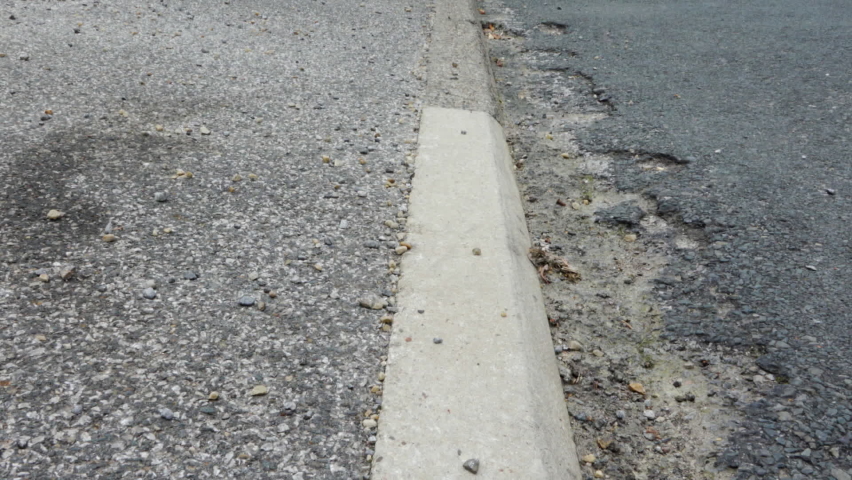 Roadside curb with potholed road surface stock footage
