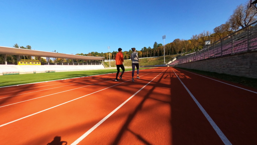 Sportive couple of motivated runners performing warming up jogging exercise running together along sport court. Stadium. Training people. FPV concept.