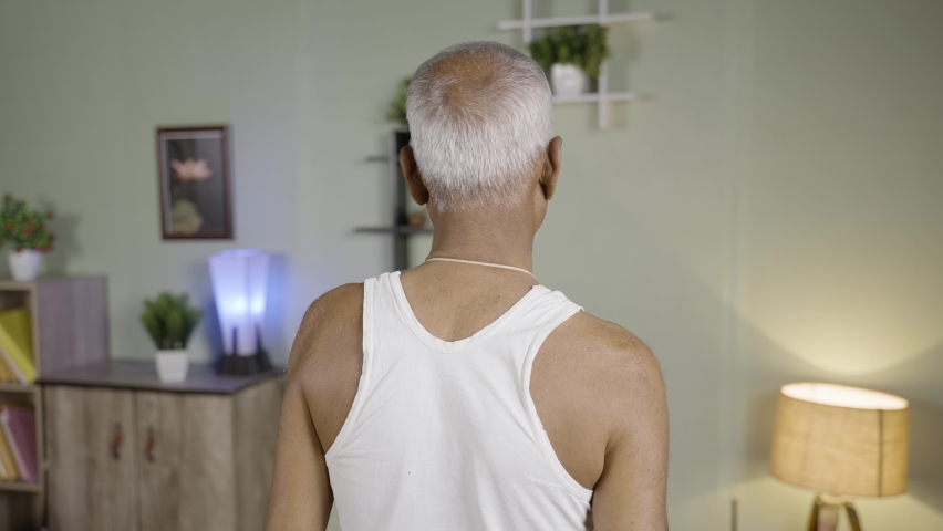 Back view of old man using Hot water bag for neck pain relief - concept of natural hot water therapy and muscle relaxtion treatment from home