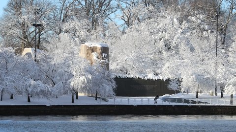 Washington, DC - USA - January 3 2022: Beautiful snow-covered Martin Luther King Jr. (MLK) memorial following a significant winter storm. The surrounding trees are white with snow. One tourist visits.