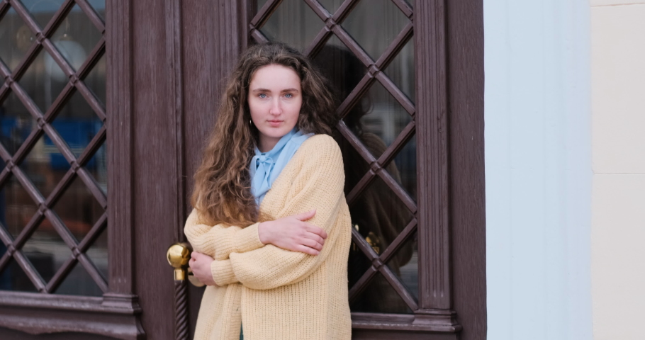 Tender young girl in a cozy sweater stands near the door, waiting. Lonely beautiful girl.