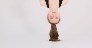 Young woman hangs upside down. Video portrait of girl headfirst on light background