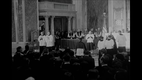 1960s: Priests kneel and pray at altar in cathedral. Cardinal blesses coffin with incense. Soldiers carry flag draped coffin from cathedral and place it on horse-drawn wagon.
