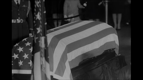 1960s: Lyndon Johnson and Jackie Onassis place flowers near flag draped coffin at President Kennedy's funeral.