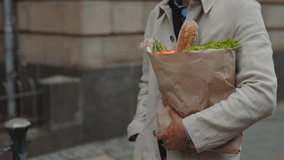 Mature man walking on city street and carrying paper bag with fresh vegetables and bread. Close up of grocery bag in male hands. - Powered by Shutterstock - Get 15% off with code: PIKWIZARD15