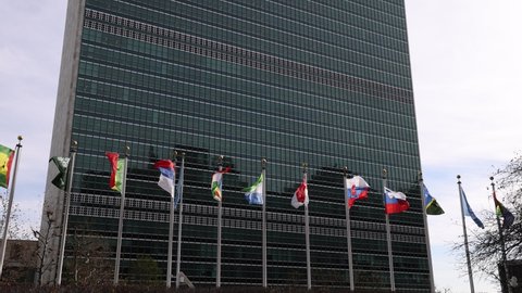 New York, USA - December 1, 2021: UN flags at United Nations Headquarters in slow motion flying at United Nations UN Secretariat building at UN HQ in NYC. UN members flags at United Nations building.