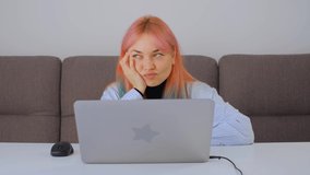 Confused girl thinking in front of laptop computer at home. Cute young woman with dyed hair trying to do work on lockdown. female expressing confusion emotion. Freelancer stock video in 4k