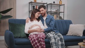 Family life. Affectionate married couple sitting in the living room. Cheerful husband hugging and kissing his pregnant wife. - Powered by Shutterstock - Get 15% off with code: PIKWIZARD15
