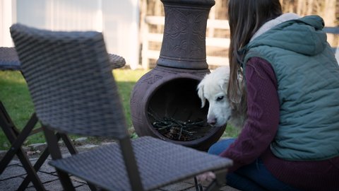 A woman and her golden retriever adding kindling to a backyard fire pit
